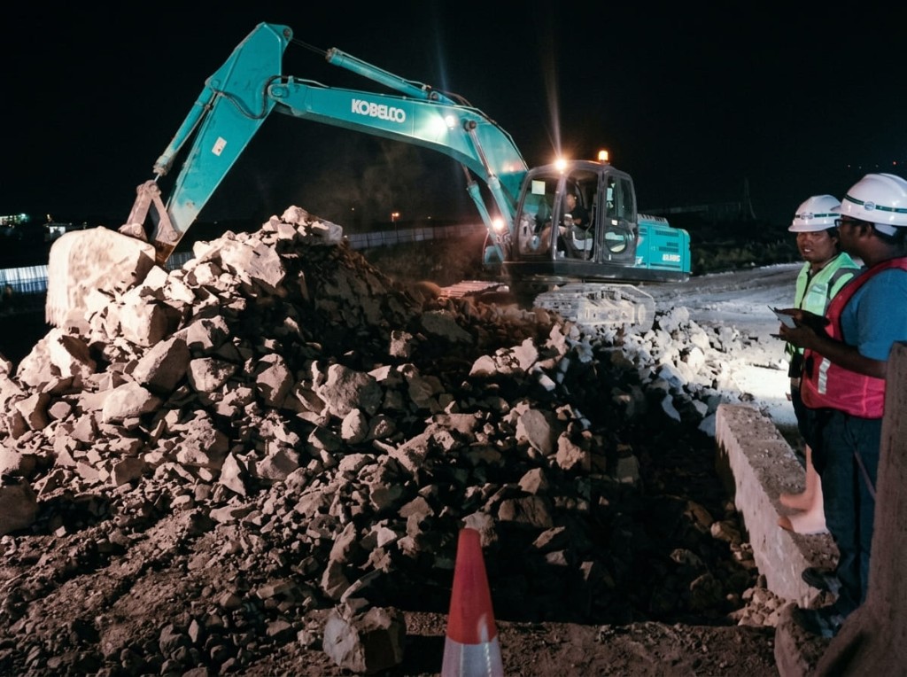 Ekskavator dan tim lapangan pada kerja malam.